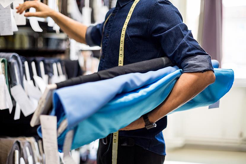 man holding bolts of fabric under arm looking at fabric on shelves