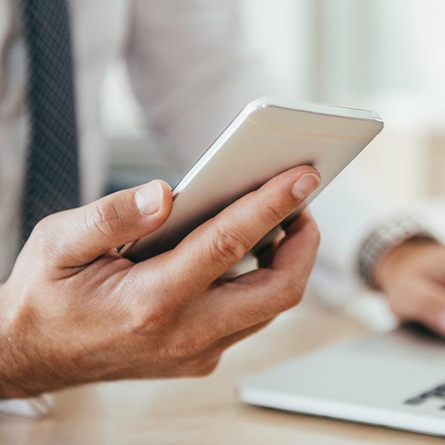 businessman holding phone in right hand left hand resting on a laptop