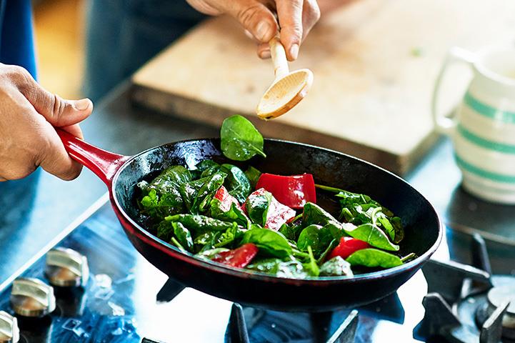 person sauteing spinach and red peppers in a skillet