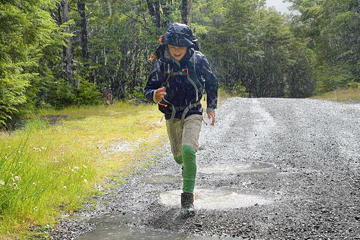 young boy wearing blue jacket running through the rain and smiling